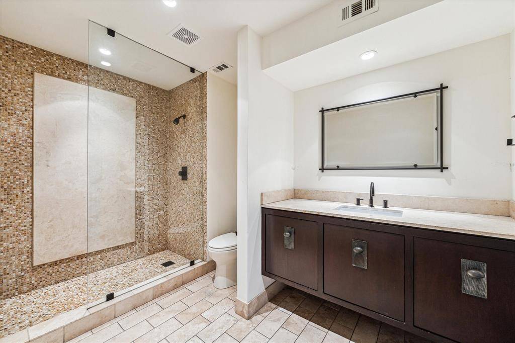 Stepping into the secondary bathroom, sleek and modern design elements immediately catch the eye. A spacious glass-enclosed shower with elegant mosaic tiling stands as the focal point.
