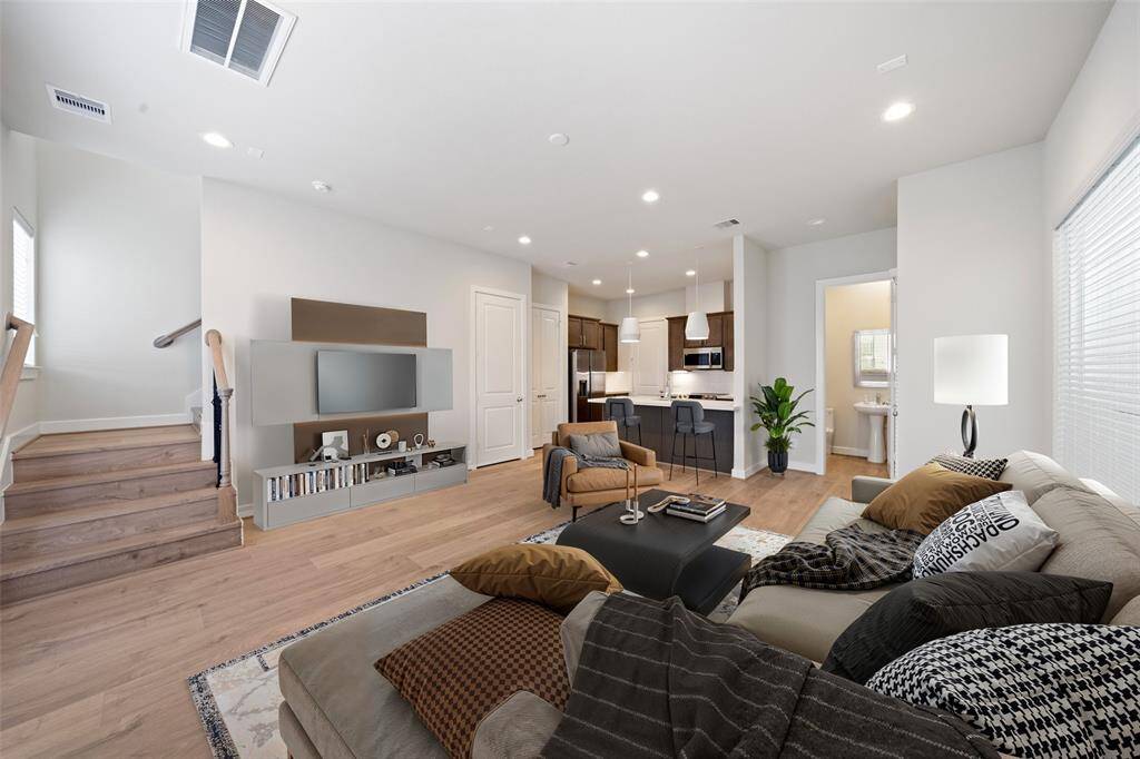 This modern, open-concept living area features a cozy seating space. The kitchen includes a breakfast bar and contemporary lighting, with a staircase leading to the upper level.