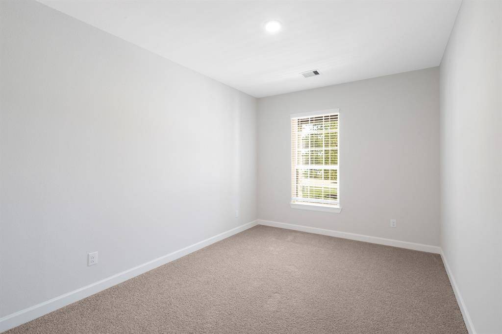 The secondary bedroom has a large window and comfortable carpet flooring.