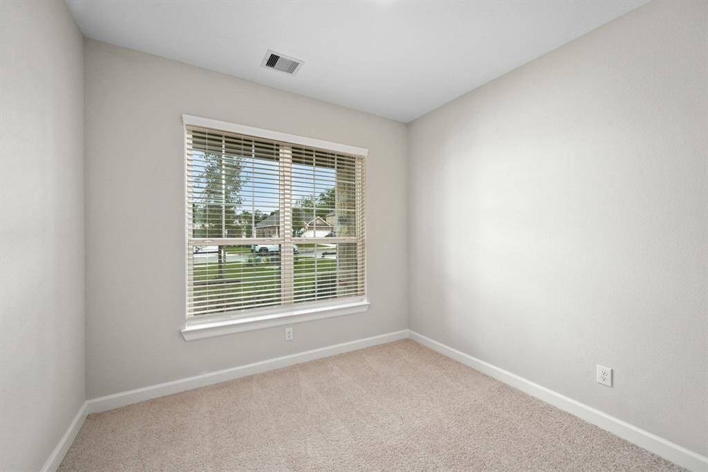 The secondary bedroom has a large window and comfortable carpet flooring.
