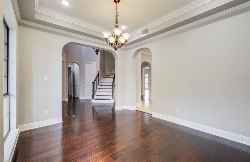 This photo showcases a bright, open entryway with elegant dark hardwood flooring, arched doorways, and a stylish chandelier. The space features crown molding and leads to a staircase, offering a welcoming and sophisticated atmosphere.