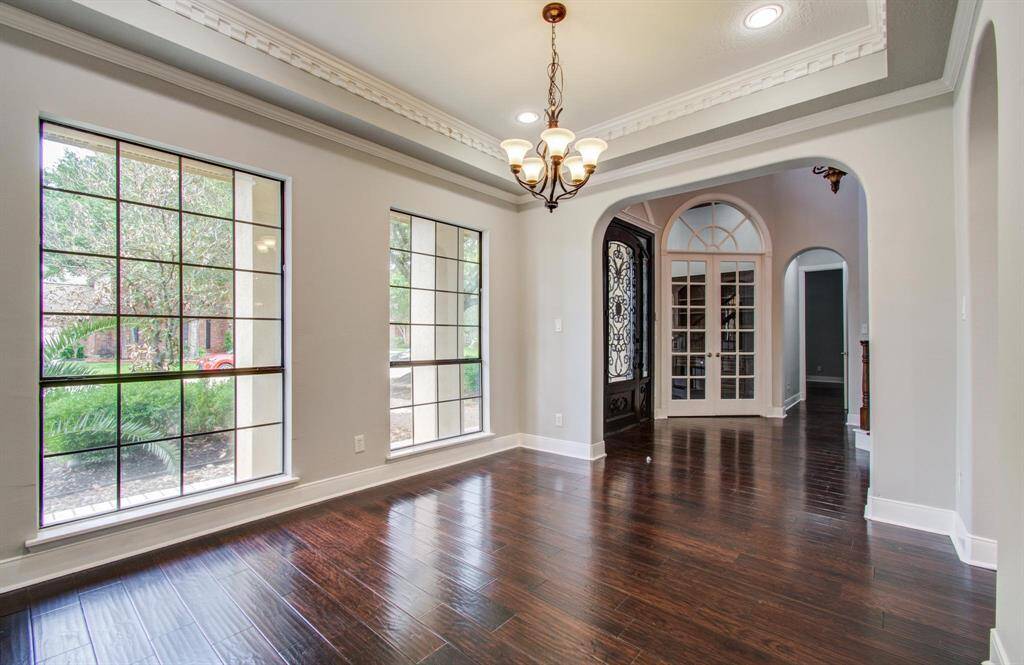 This spacious entryway features dark hardwood floors, large windows for natural light, and elegant crown molding. The area is enhanced by stylish arches, a decorative chandelier, and a grand front door with intricate glass design, creating an inviting atmosphere.