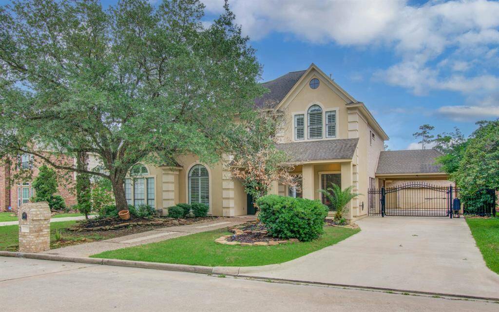 This charming two-story home features a classic exterior with large arched windows, a well-maintained front yard with mature trees, and a gated driveway leading to a detached garage. Perfect for family living in a serene neighborhood.