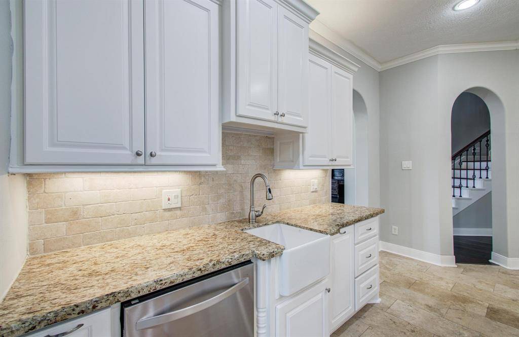 This kitchen features elegant white cabinetry, granite countertops, and a farmhouse sink. The neutral tile backsplash and flooring add a classic touch, while arched doorways provide architectural interest.
