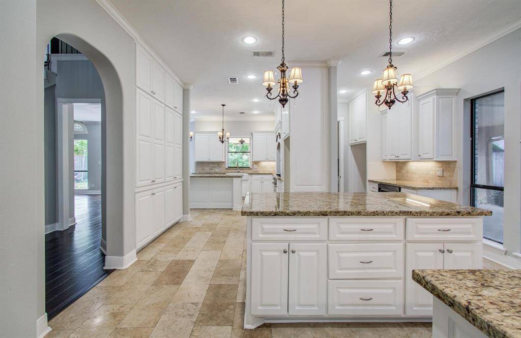 This kitchen features elegant white cabinetry, granite countertops, and a spacious island. It includes stylish pendant lighting and ample storage, with an open layout that connects to other living spaces.