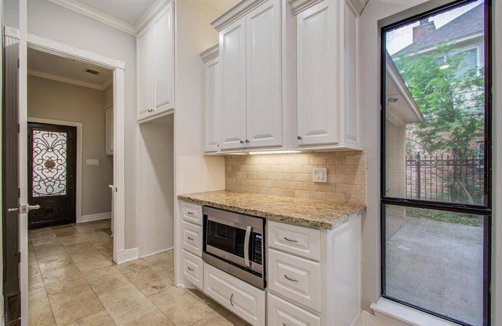 This photo shows a bright kitchen area with white cabinetry, granite countertops, and a built-in microwave. It features a large window providing natural light and a view outside, along with a decorative door leading to another room.