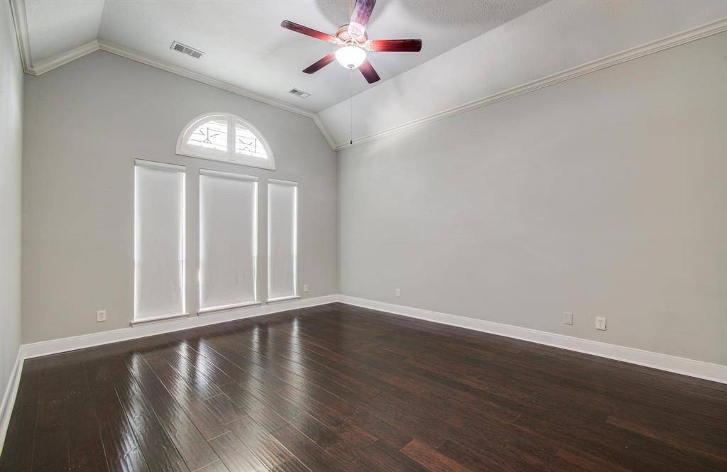 This room features high ceilings, a large arched window for natural light, sleek dark wood flooring, and a modern ceiling fan, offering a spacious and contemporary feel.