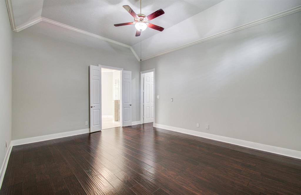 This spacious room features dark hardwood floors, light gray walls, and a high ceiling with a ceiling fan. Double doors lead to an adjoining area, enhancing the open feel.