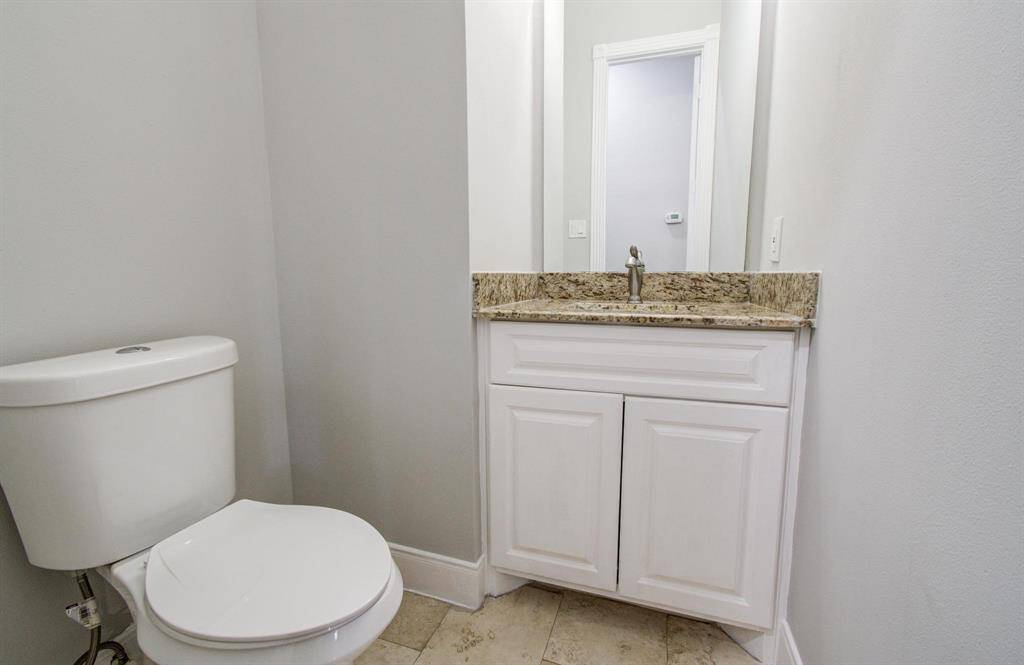 This is a compact bathroom featuring a toilet and a vanity with a granite countertop, set against light-colored walls and tile flooring.