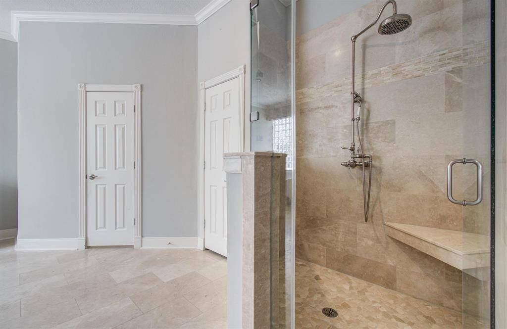 This bathroom features a spacious, modern walk-in shower with elegant tile work and a rainfall showerhead. The room is bright, with light-colored walls and flooring, and includes two paneled doors, adding to the sleek, contemporary design.