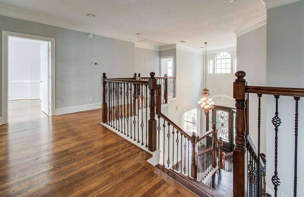 This photo showcases a bright and airy upstairs landing with elegant dark wood flooring and decorative iron railings. It overlooks a grand foyer with a large chandelier and impressive arched windows, creating a welcoming entrance.