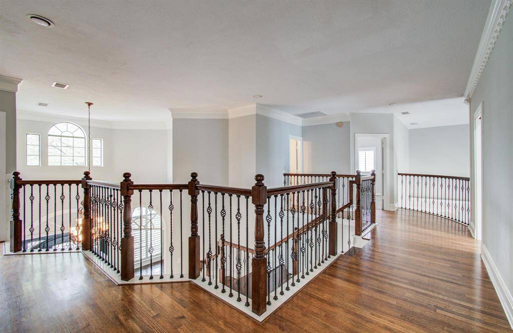 This photo showcases a spacious upstairs landing with elegant hardwood floors and decorative wrought iron railings. The area is well-lit with natural light from large windows, creating a bright and airy atmosphere.