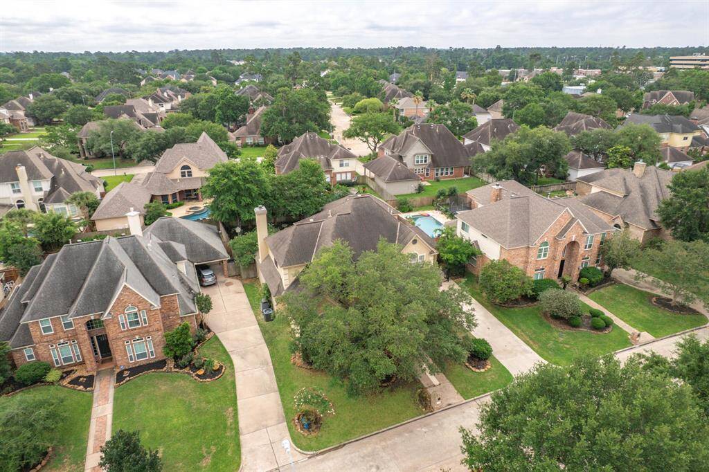 This aerial view showcases a picturesque suburban neighborhood with spacious, well-maintained brick homes, landscaped yards, and tree-lined streets, offering a peaceful and inviting atmosphere.