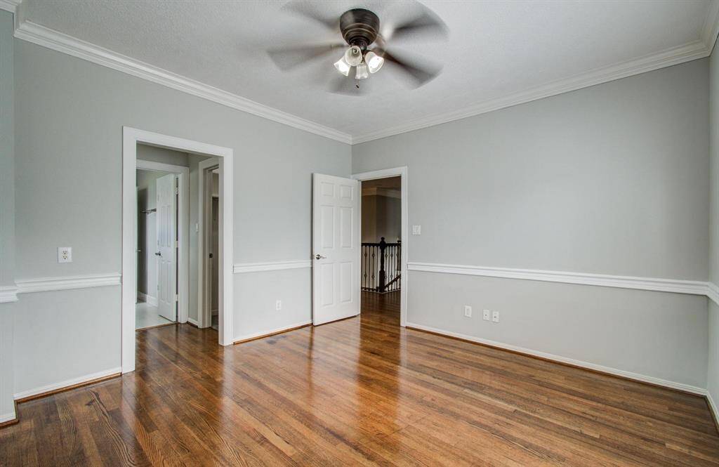 Bright room with hardwood floors, light gray walls, white trim, and a ceiling fan. Features two doorways leading to other areas, offering a versatile space.