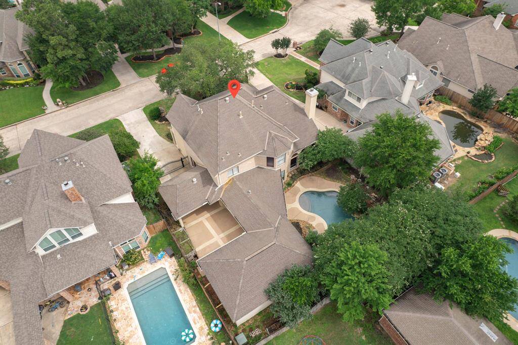 This aerial photo showcases a spacious two-story home with a well-maintained roof, surrounded by lush greenery. The property features a private backyard with a swimming pool and ample patio space. It's situated in a quiet, tree-lined neighborhood with nearby homes of similar size and style.