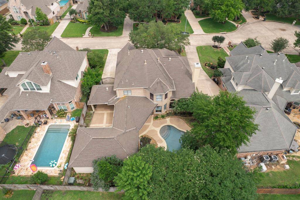 This aerial view showcases a spacious two-story home with a unique, curved swimming pool in a well-maintained backyard. The neighborhood is peaceful and suburban, with tree-lined streets and nearby homes featuring similar architectural styles.