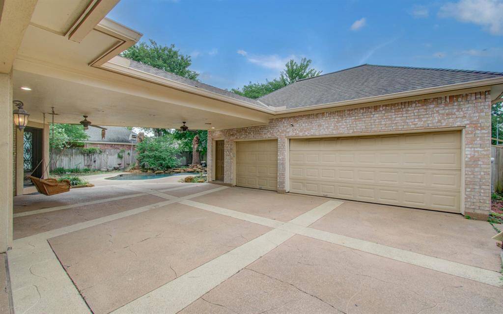 This photo showcases a spacious driveway with a three-car garage, covered patio area with ceiling fans, and a swing. The space leads into a backyard featuring greenery and a small pool, creating an inviting outdoor area perfect for relaxation and entertainment.
