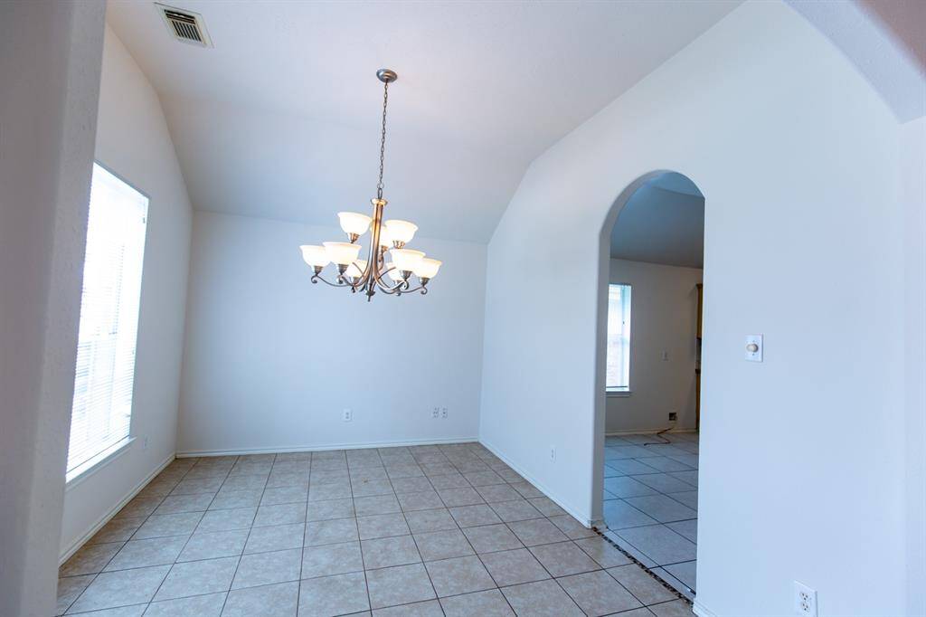 The dining area with tile flooring and an arched entryway leading to another kitchen. A large window offers natural light and high ceiling, enhancing the room's airy feel.