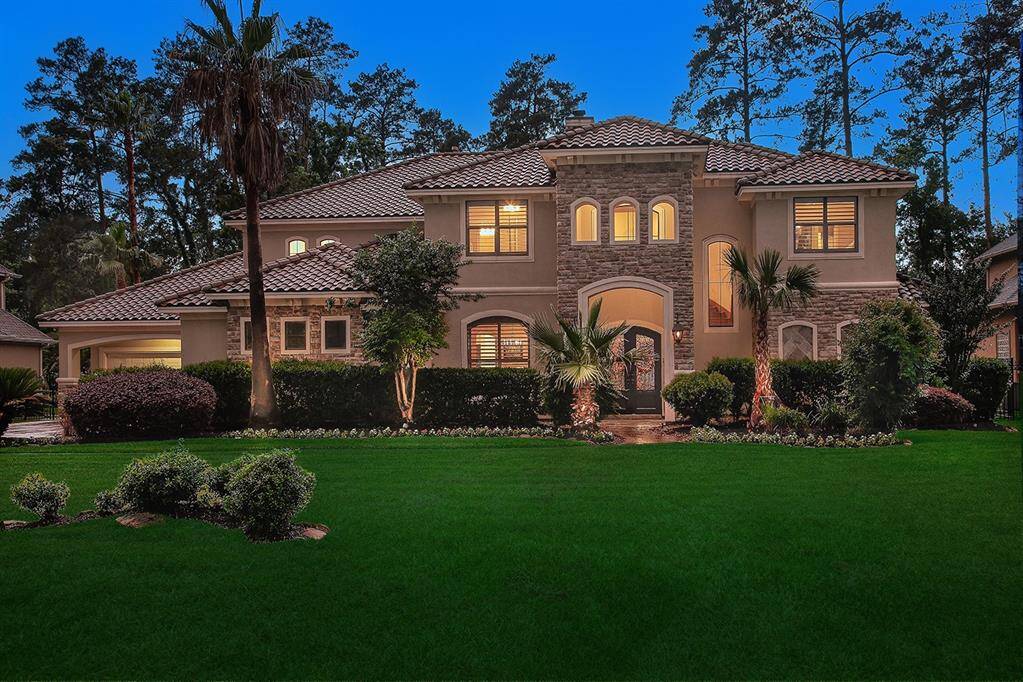Stunning two-story home with a Mediterranean-style design, showcasing a mix of stucco and stone accents. The property is surrounded by lush landscaping, including palms and manicured hedges, set against a backdrop of the acclaimed Augusta Pines Golf Course.