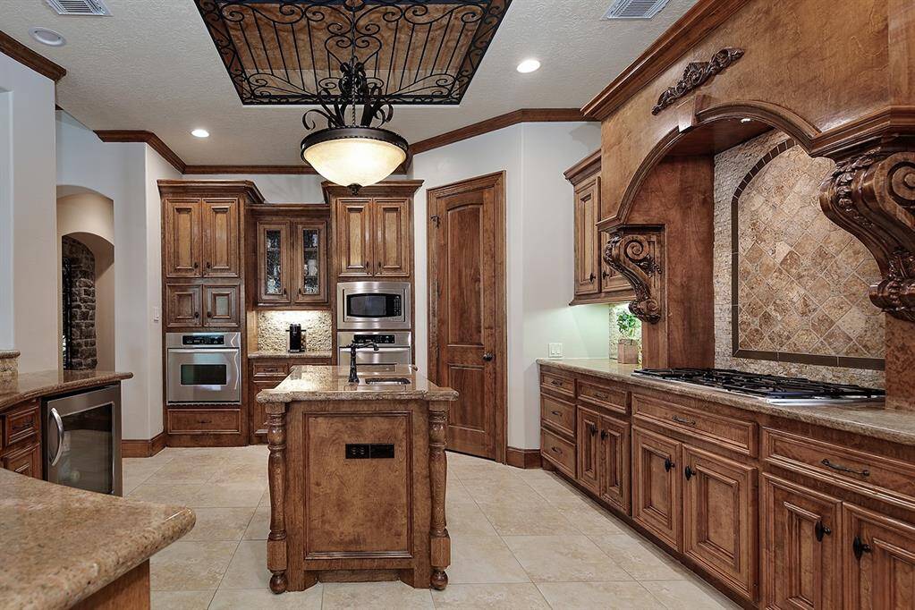 Large kitchen features custom cabinetry, a central island, and modern stainless steel appliances. The tiled backsplash complements the warm tones, and a decorative ceiling light and ceiling accent add to the elegance of the space.