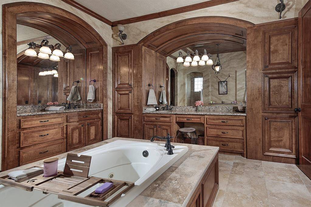 Elegant bathroom features a large soaking tub, dual sinks with granite countertops, and rich wood cabinetry. The arched mirrors and lighting accents add a touch of luxury, while the tiled floor completes the sophisticated look.