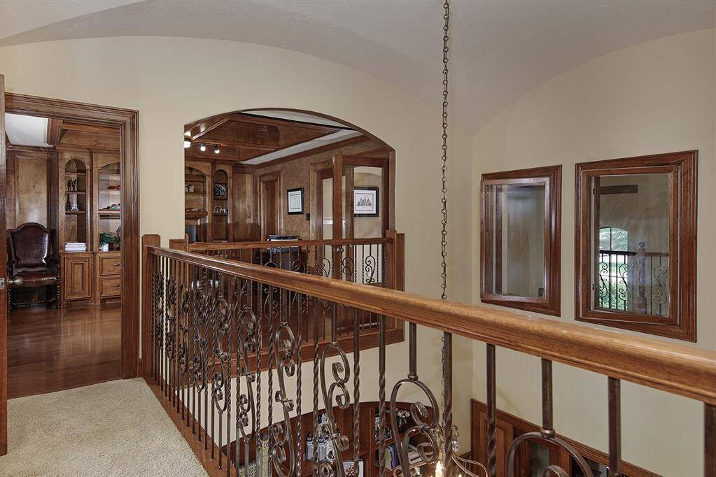 Elegant upstairs hallway with wrought iron railing, leading to a wood-paneled office overlooking the den/library.