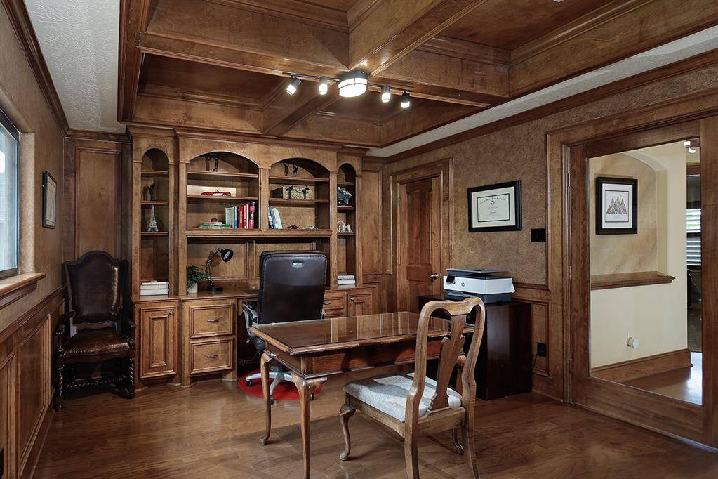 Stately home office with rich wood paneling and built-in desk and shelves. The room features an impressive coffered ceiling, closet and amazing golf course views.