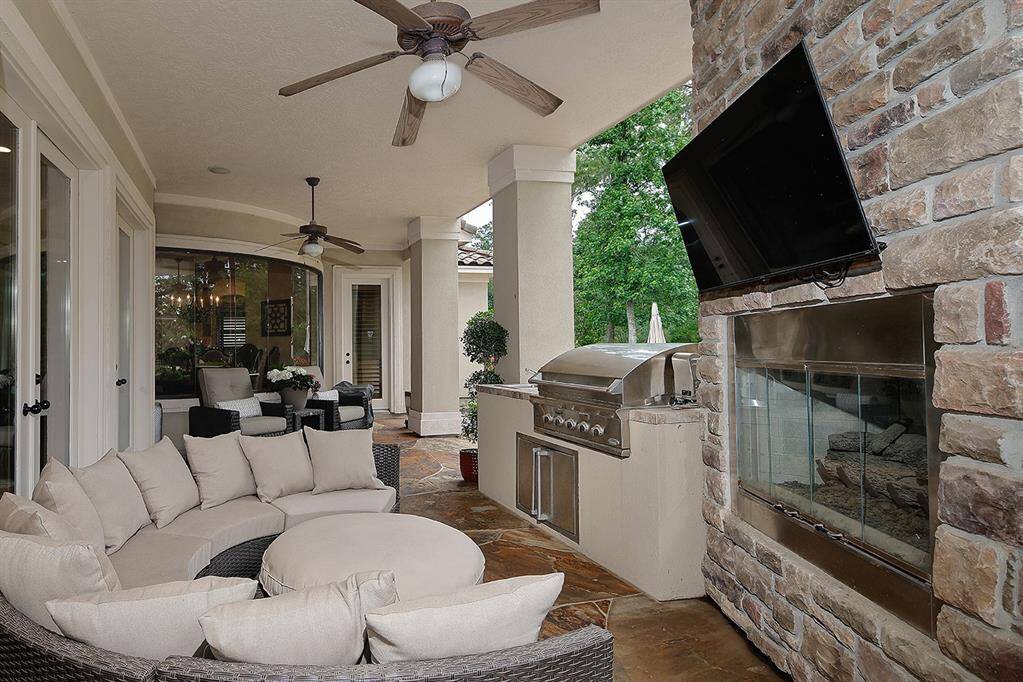 Stylish outdoor living and dining area with cozy stone fireplace and TV mounting, perfect for entertaining while the grill master is at work.