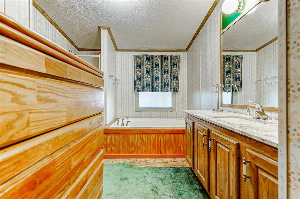 Primary bathroom offers warm wood finishes, granite countertop, & soaking tub for a tranquil retreat.