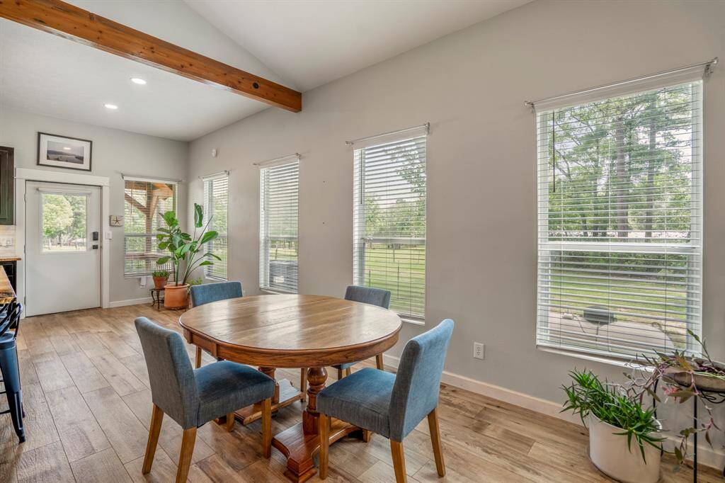 This dining area features a warm, inviting space with large windows offering ample natural light and views of lush greenery. The exposed beam adds a rustic charm, over a cozy setting for meals.