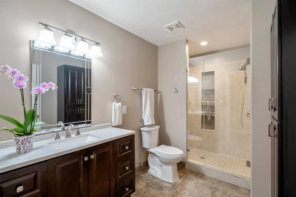 The secondary bathroom showcases a glass-enclosed shower, tile flooring, and a sleek vanity with a large mirror.