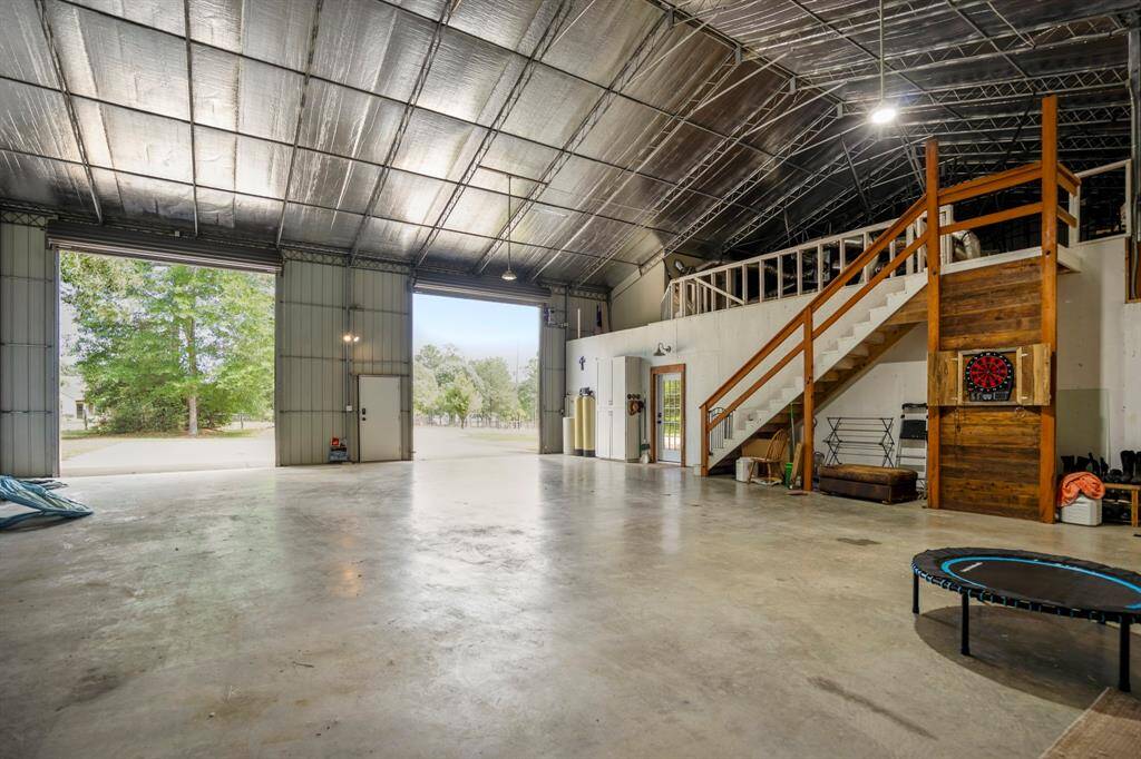This spacious building features high ceilings and concrete floors, ideal for storage or a workshop. There's ample room for vehicles, equipment, and more. A staircase leads to an upper level, adding versatility to the space.