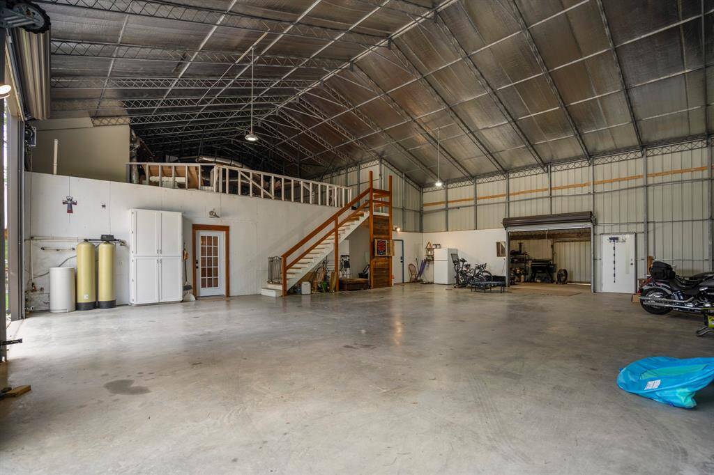Spacious multi-purpose garage space with high ceilings, large roll-up doors, and a lofted area accessible by stairs. Ideal for storage, workshops, or recreational use, with ample natural light and easy outdoor access.