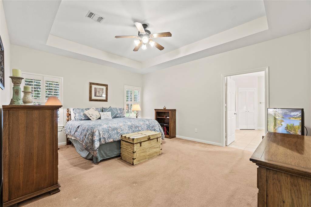 The spacious primary bedroom boasts a sophisticated coffered ceiling, elegant shutters, and a private ensuite bath, creating a serene and luxurious retreat.