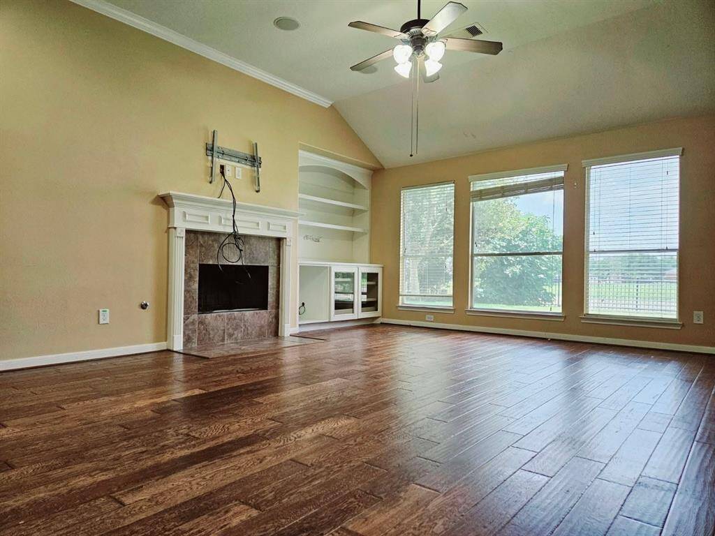 This expansive living area features rich wood flooring, a cozy fireplace, and a ceiling fan overhead. A wall of large windows draws in serene lake views, adding a picturesque backdrop to the space.