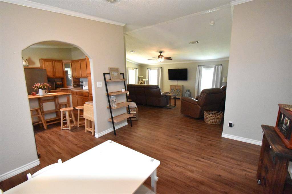 This inviting living space features an open floor plan, a cozy lounge area and a wall-mounted TV. The archway leads to a kitchen with wooden cabinets and a breakfast bar, creating a warm and functional layout.