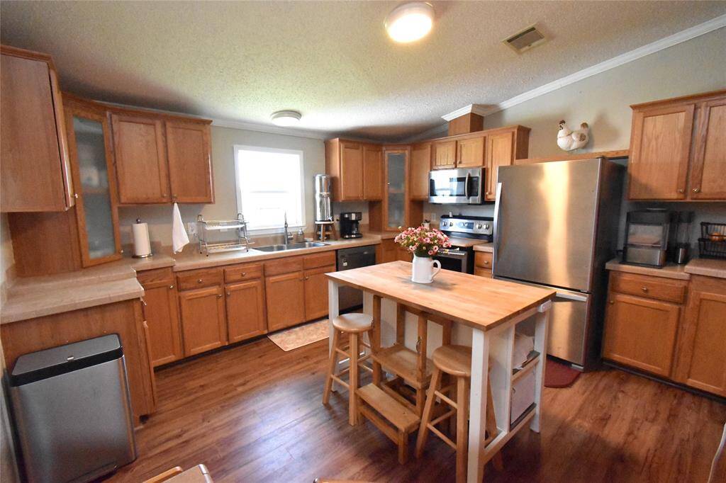 This kitchen features warm wooden cabinetry, stainless steel appliances, and a central island with seating. The space is well-lit with natural light from the window, and there's ample counter space for cooking and storage.