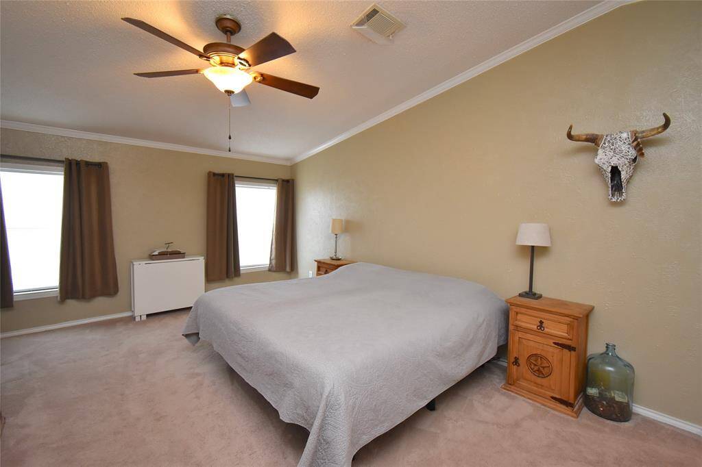This bedroom features a cozy atmosphere with neutral walls, a ceiling fan, and two large windows providing natural light. It includes carpeted flooring.
