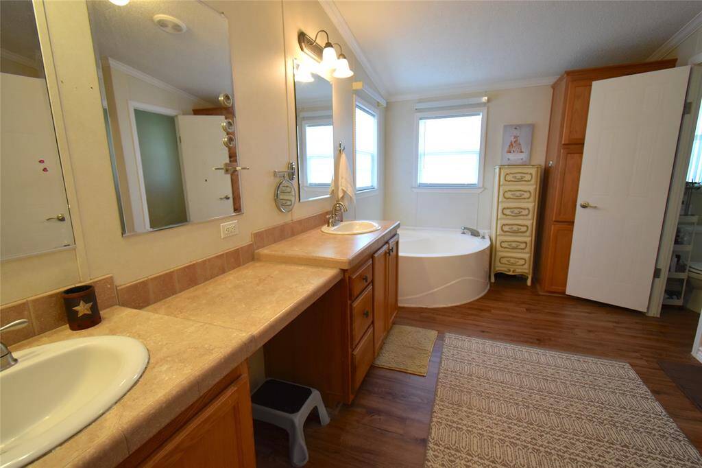 This spacious bathroom features a large corner bathtub, dual sinks with ample counter space, and warm wood cabinetry. Natural light streams in through two windows, which enhances the cozy ambiance.