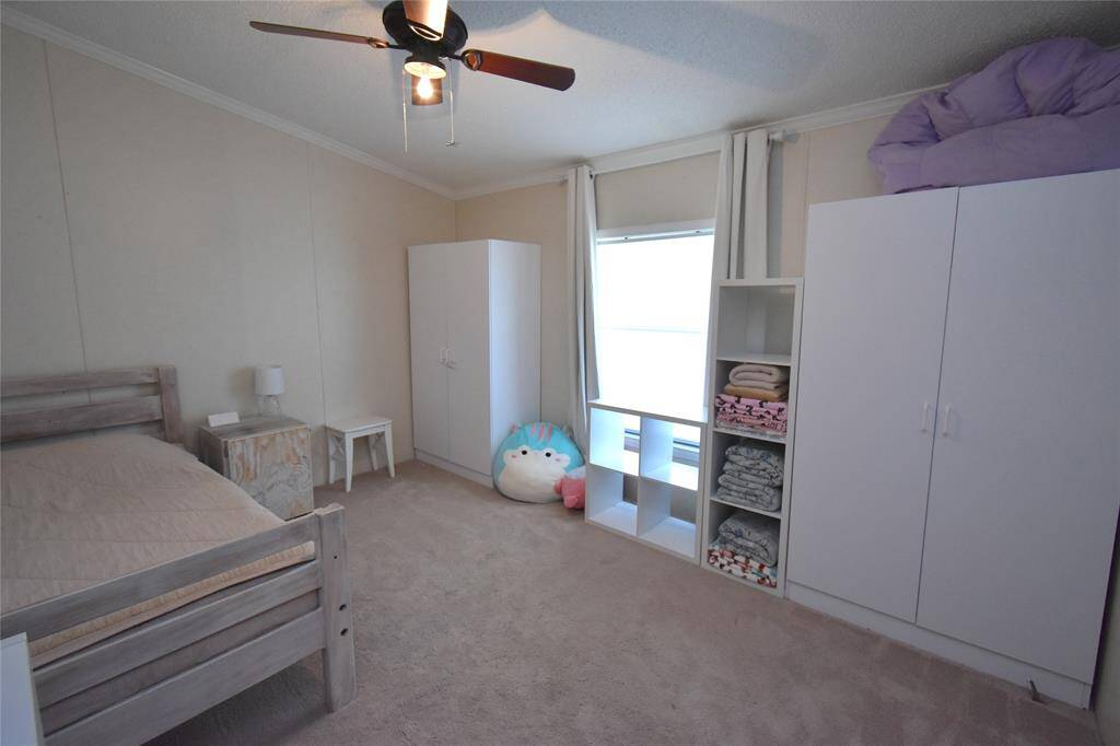 This cozy bedroom features neutral walls, carpeted flooring, and a ceiling fan. Ample storage with white cabinets and open shelves. A large window provides natural light, making the space bright and welcoming.