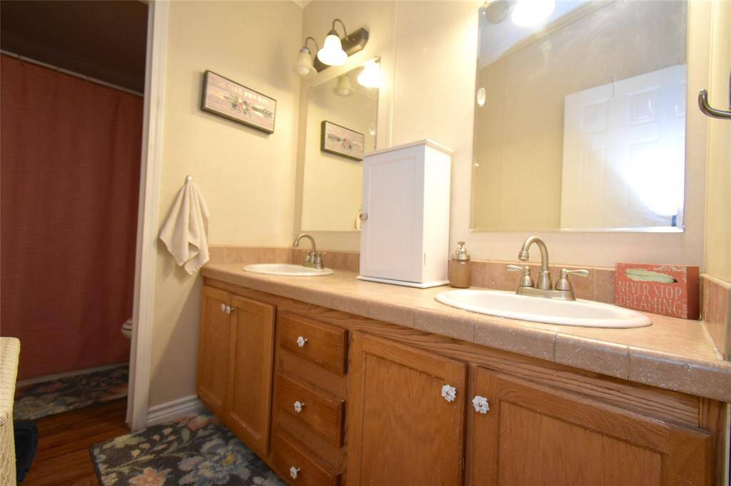 This bathroom features a double sink vanity with wooden cabinets, a large mirror, and warm lighting.