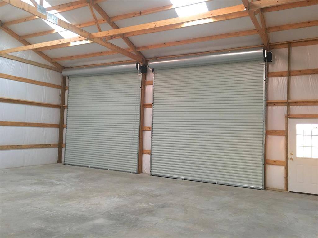 Spacious garage or workshop with high ceilings, featuring 3 large roll-up doors and a side entry door. Ideal for storage or projects.