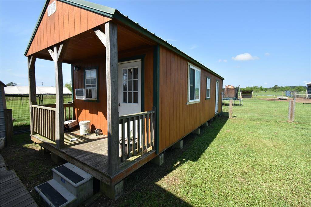 This photo shows a small, rustic school house cabin with a wooden porch and steps, situated on a spacious lot. The cabin features a roof and windows, offering a cozy retreat feel amidst open, rural surroundings.