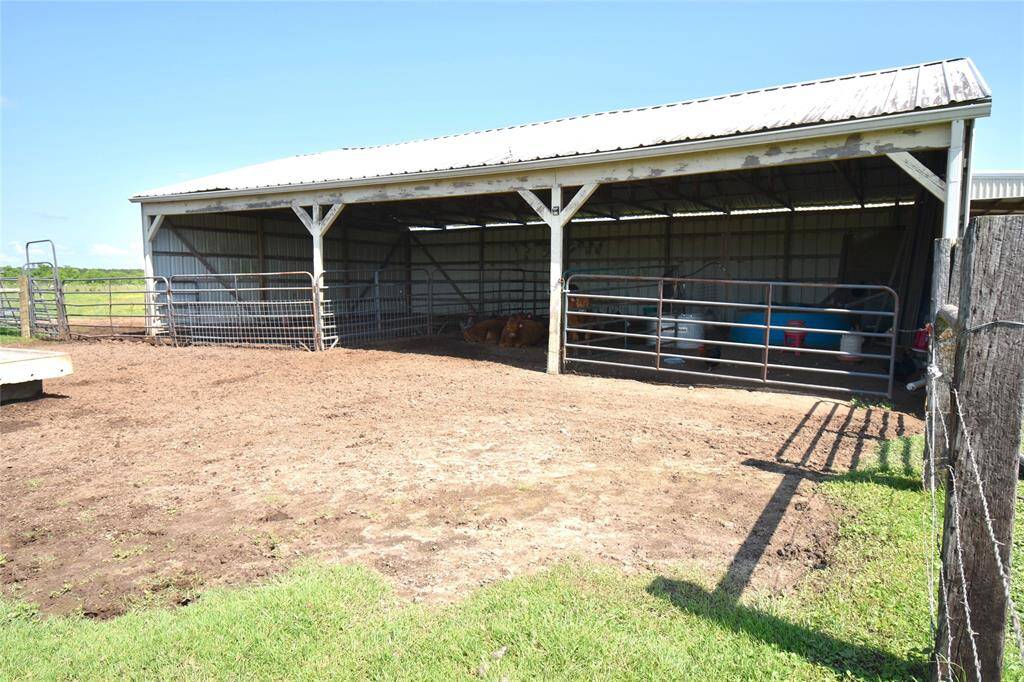 Metal livestock shelter with a fenced enclosure, ideal for housing your farm animals. The structure provides ample shade and protection, with open sides for ventilation, set within a rural, grassy area.