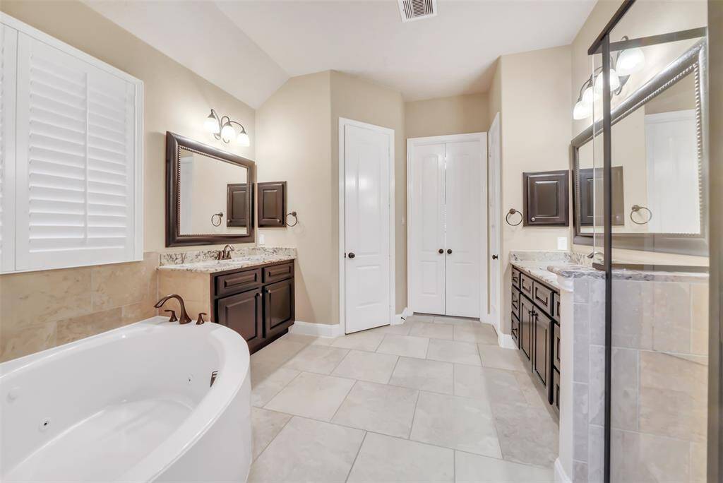 Dual sinks, set in elegant granite countertops, offer ample space for daily routines. The rich, dark wood cabinetry enhances the bathroom's sophisticated charm, complementing the neutral tile flooring and walls.