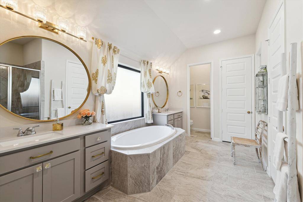 The light-filled, spa-like primary bathroom features a garden tub and separate walk-in shower, walk-in closet, linen closet and two SEPARATE vanities.  The 40-inch round framed mirrors and upgraded vanity lights add a touch of glam to the bathroom!