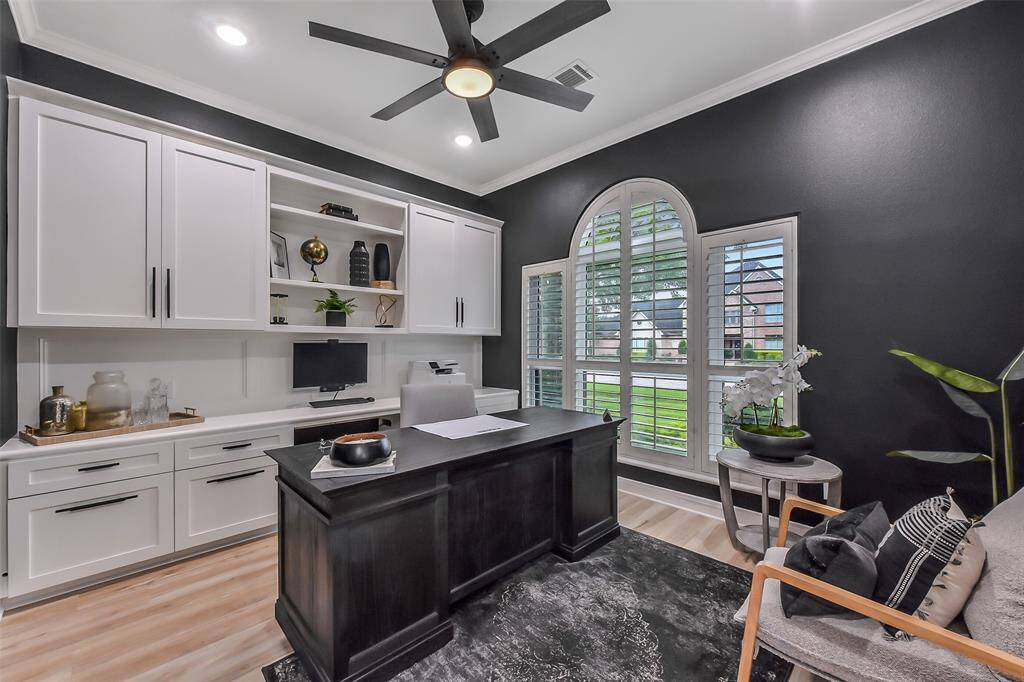 Elegant home office featuring custom cabinetry, modern lighting, and a large arched window with plantation shutters. Ideal for productivity and style.