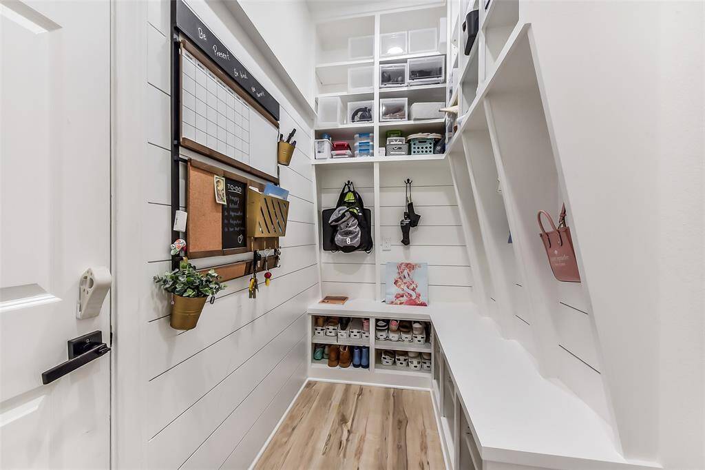 This photo showcases a well-organized mudroom with white shiplap walls, built-in storage cubbies, a bench, shoe shelves, and a wall-mounted organizer with a chalkboard and corkboard for notes. I’mIdeal for keeping your entryway tidy and efficient.