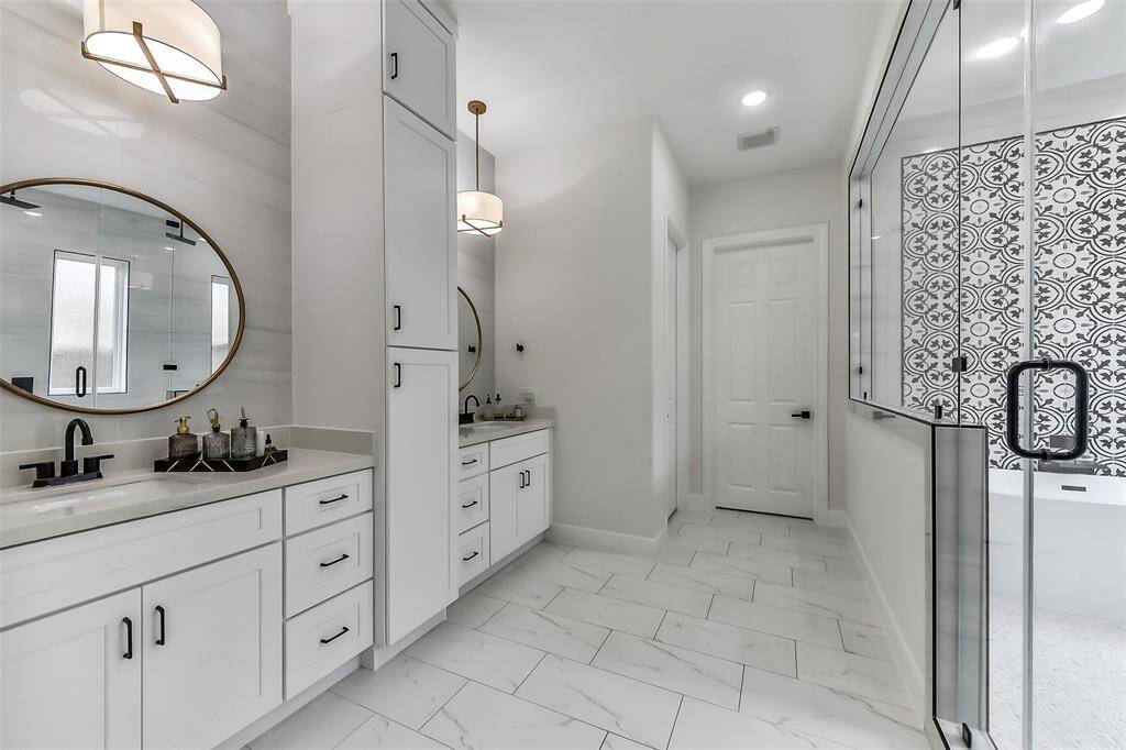Discover elegance in this modern bathroom featuring dual vanities, chic round mirrors, and sleek black fixtures. Enjoy the spacious walk-in shower adorned with stylish patterned tiles, complemented by bright, airy lighting. Perfect for luxurious relaxation.