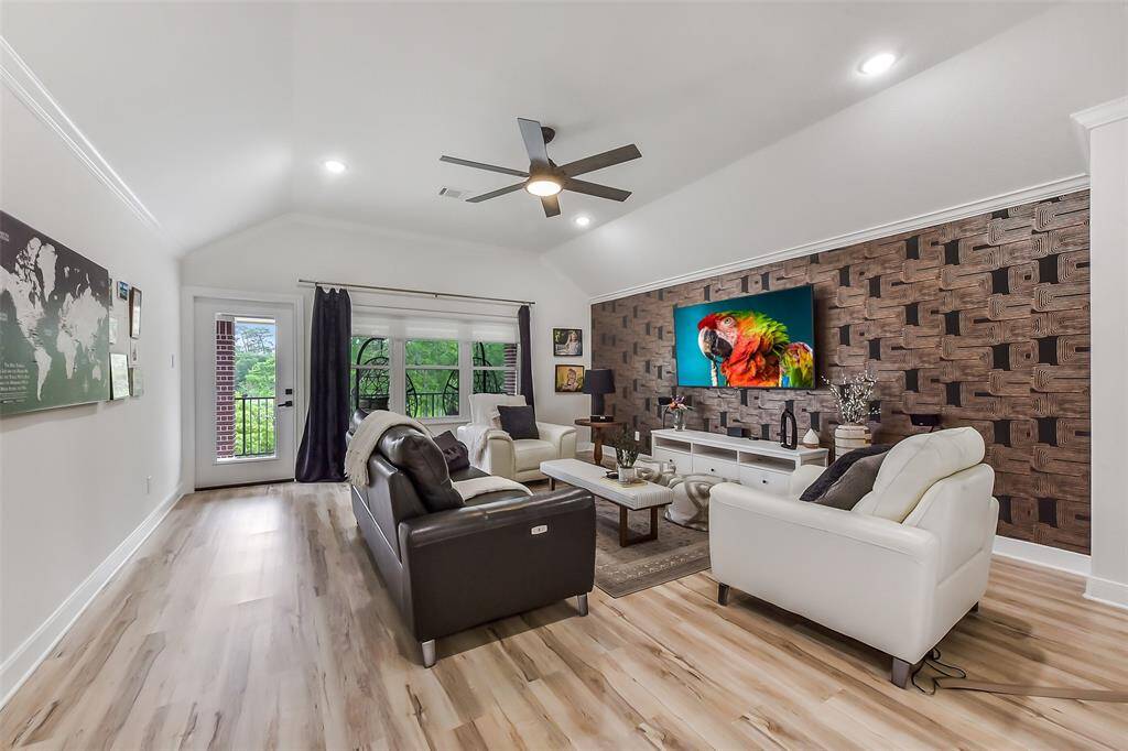 This spacious living room features a high ceiling with a modern fan, stylish wood-patterned accent wall, and large windows for natural light.